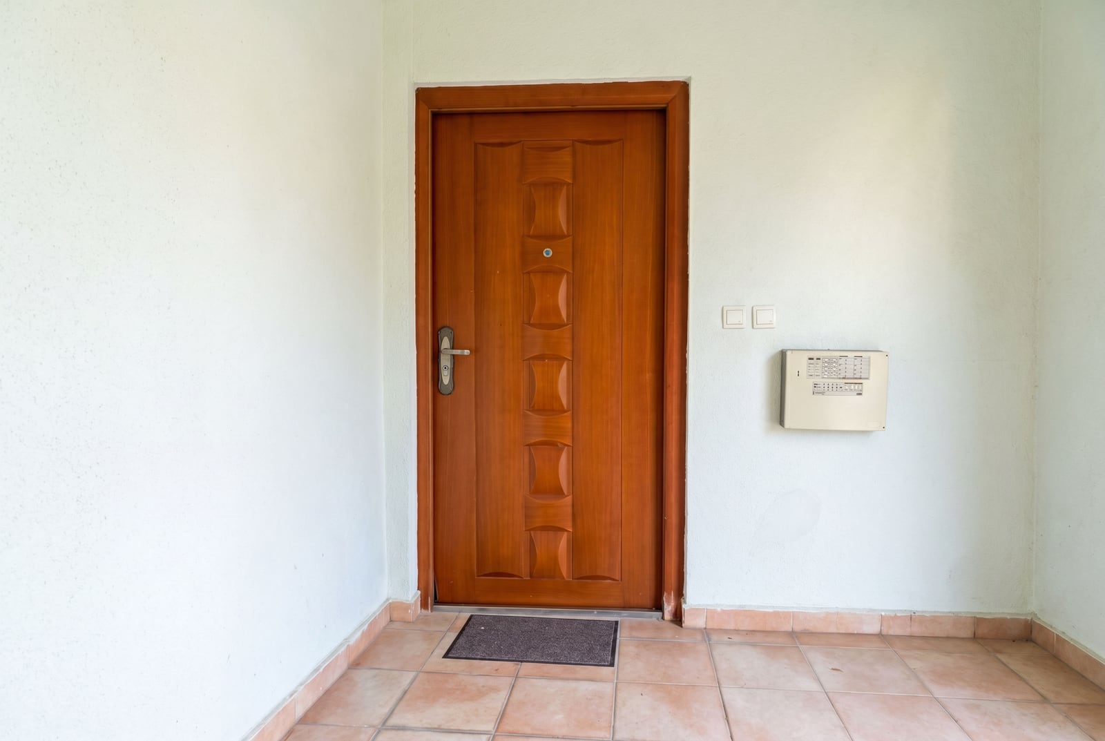 Wooden entrance door to an apartment in Budva, Montenegro: light-colored walls, tiled floor, and an intercom in the hallway.