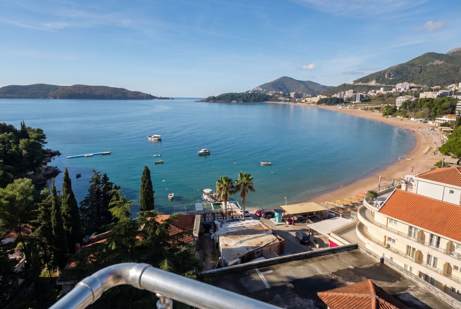 Panoramic view from the apartment balcony in Rafailovici, Montenegro: sandy beach, azure sea, and mountains.