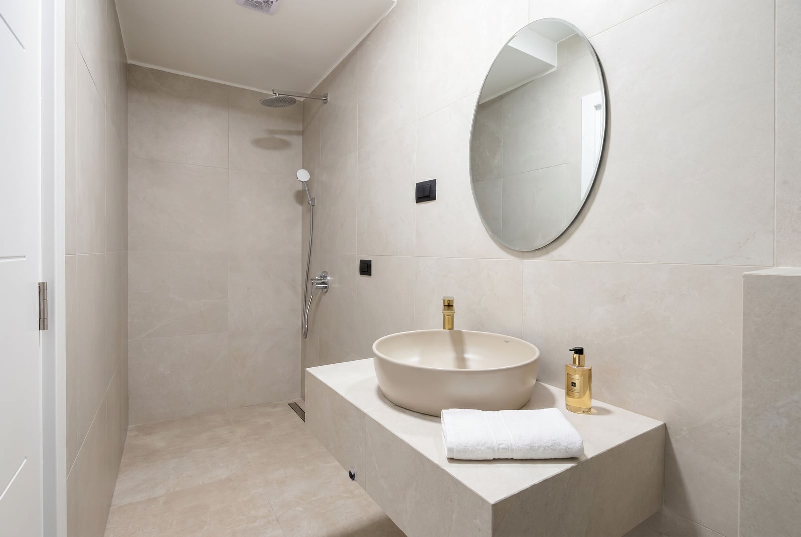 Modern indoor bathroom, Budva, Montenegro: beige tiles, round mirror, and vessel sink.