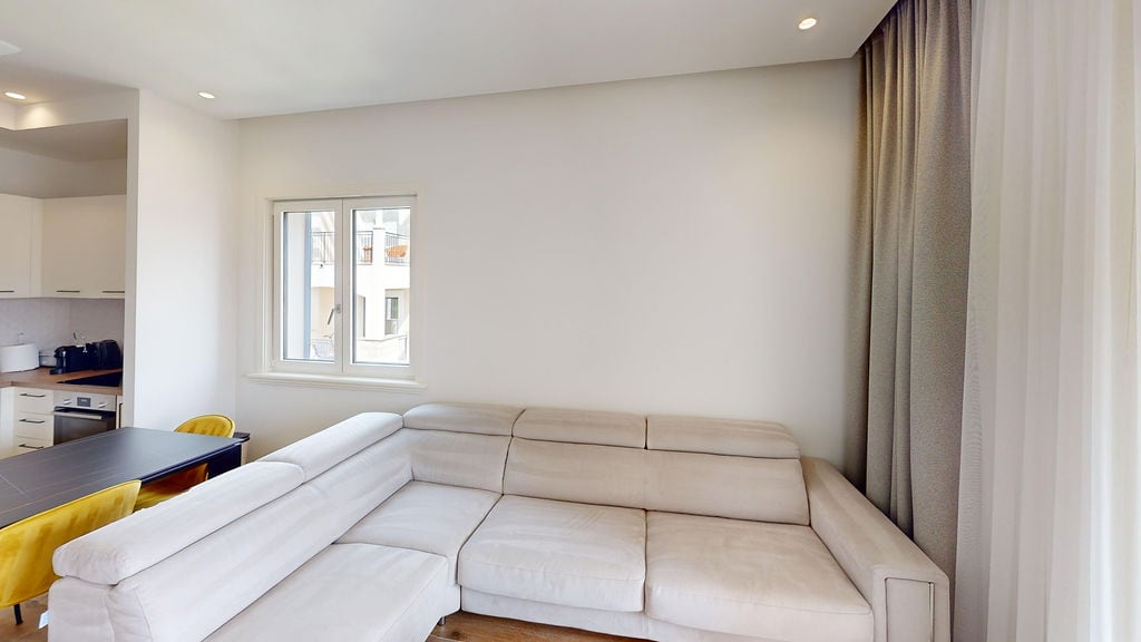 Bright living room with a corner sofa and kitchen in the Lustica Bay apartments, Montenegro. Modern interior with panoramic windows...