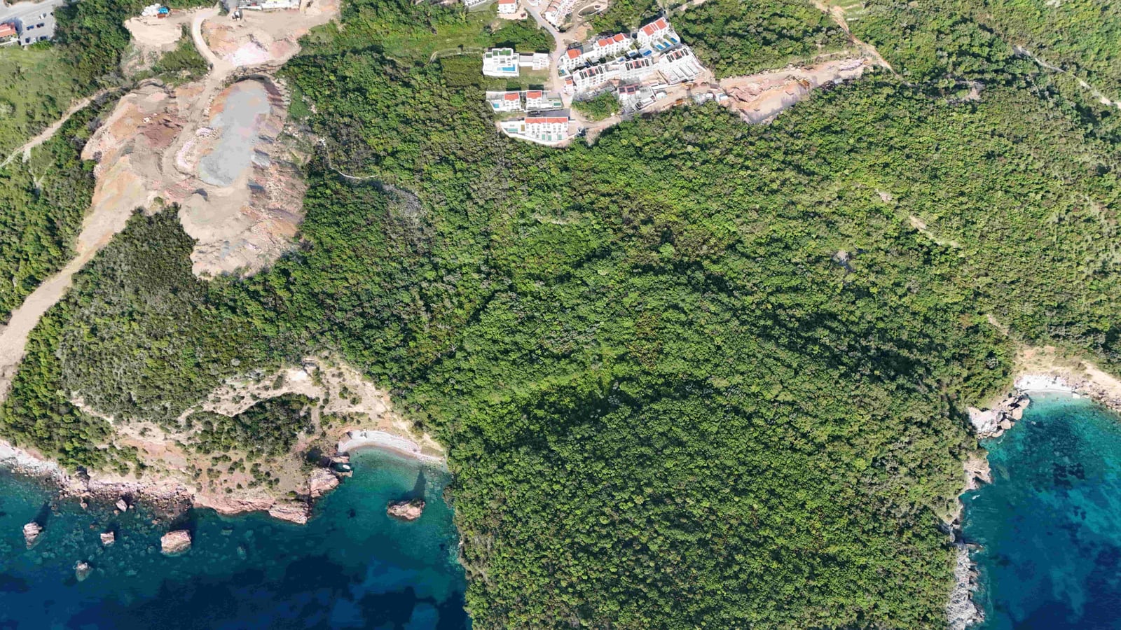 Aerial view of a land plot in Reževići, Montenegro: a forested area by the sea with a beach and nearby development.