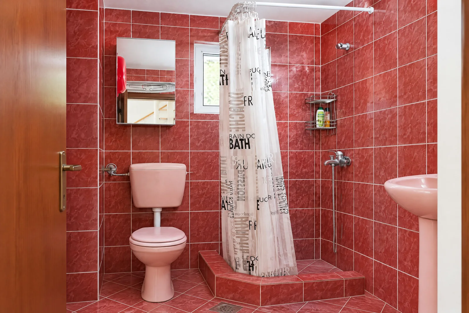 Bathroom with red tiles, pink toilet, sink, and shower area separated by a printed curtain.