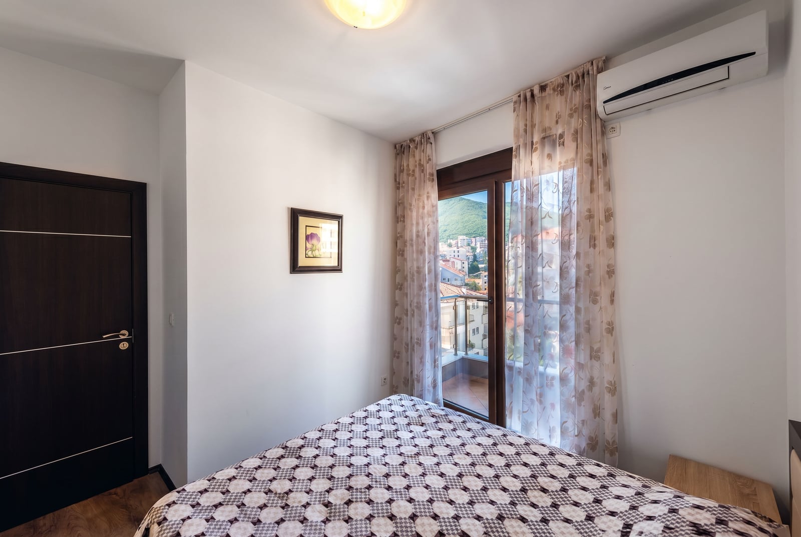 Cozy bedroom in an apartment in Budva, Montenegro: double bed, balcony access with mountain and city views.