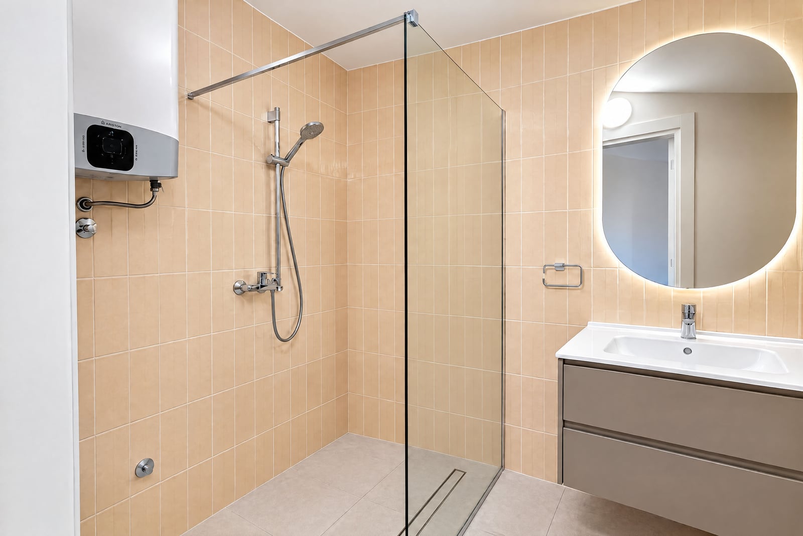 Modern bathroom featuring a glass shower enclosure, beige wall tiles, a vanity sink, and a backlit round mirror.