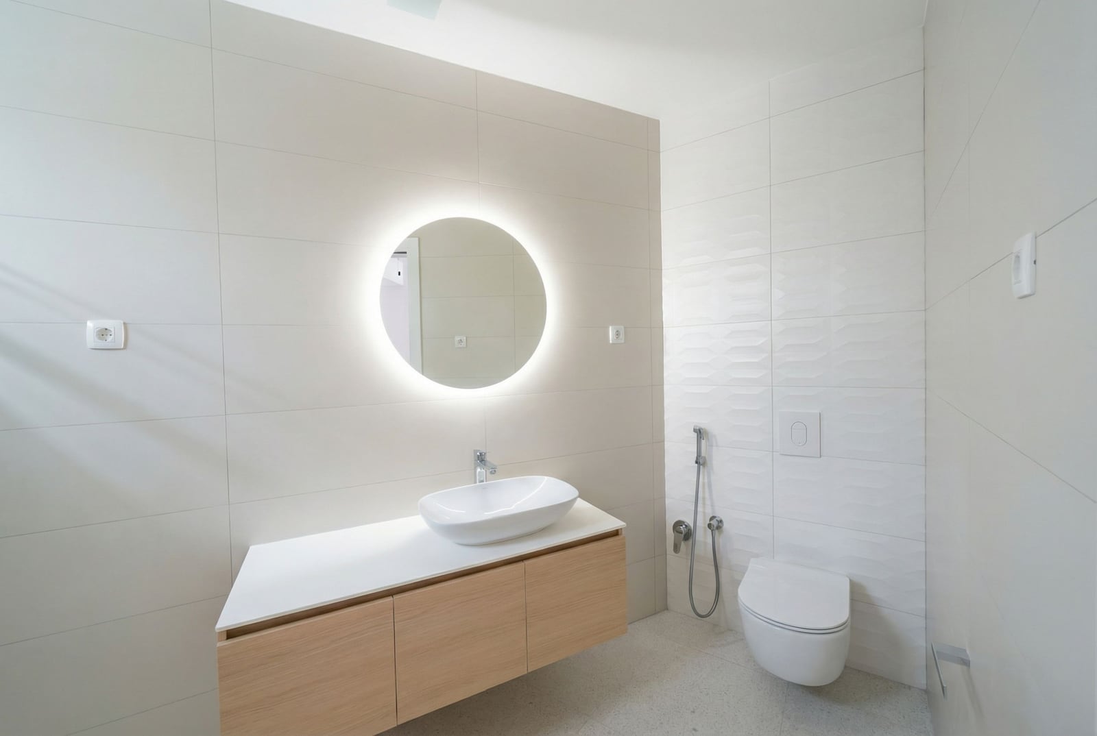 Modern bathroom in an apartment in Bečići, Montenegro: wall-mounted vanity, round backlit mirror, and shower.