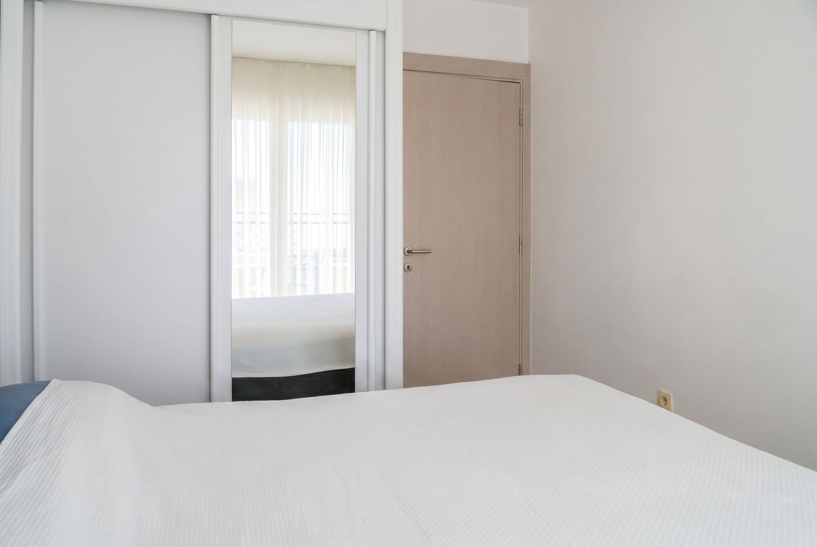 Modern bedroom with white furniture, mirrored wardrobe, and light finishes in an apartment in Budva, Montenegro