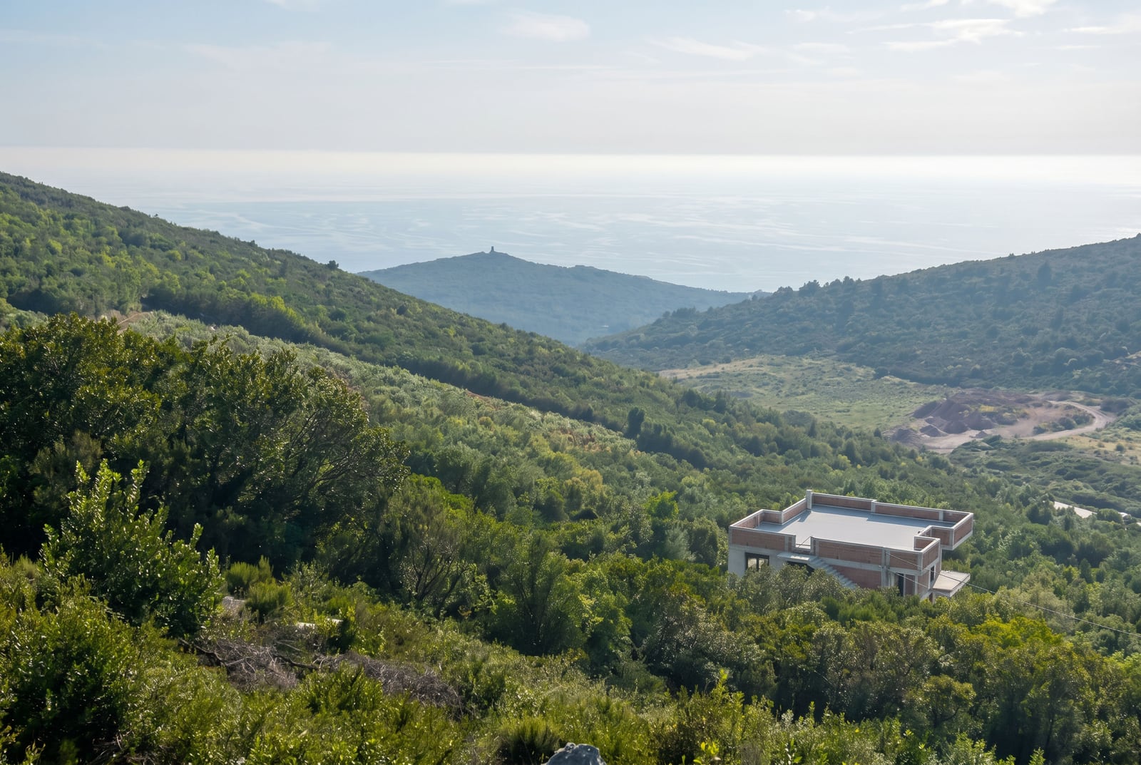House under construction on a plot of land in the mountains of Budva, Montenegro, with a panoramic view of the sea and green hills.