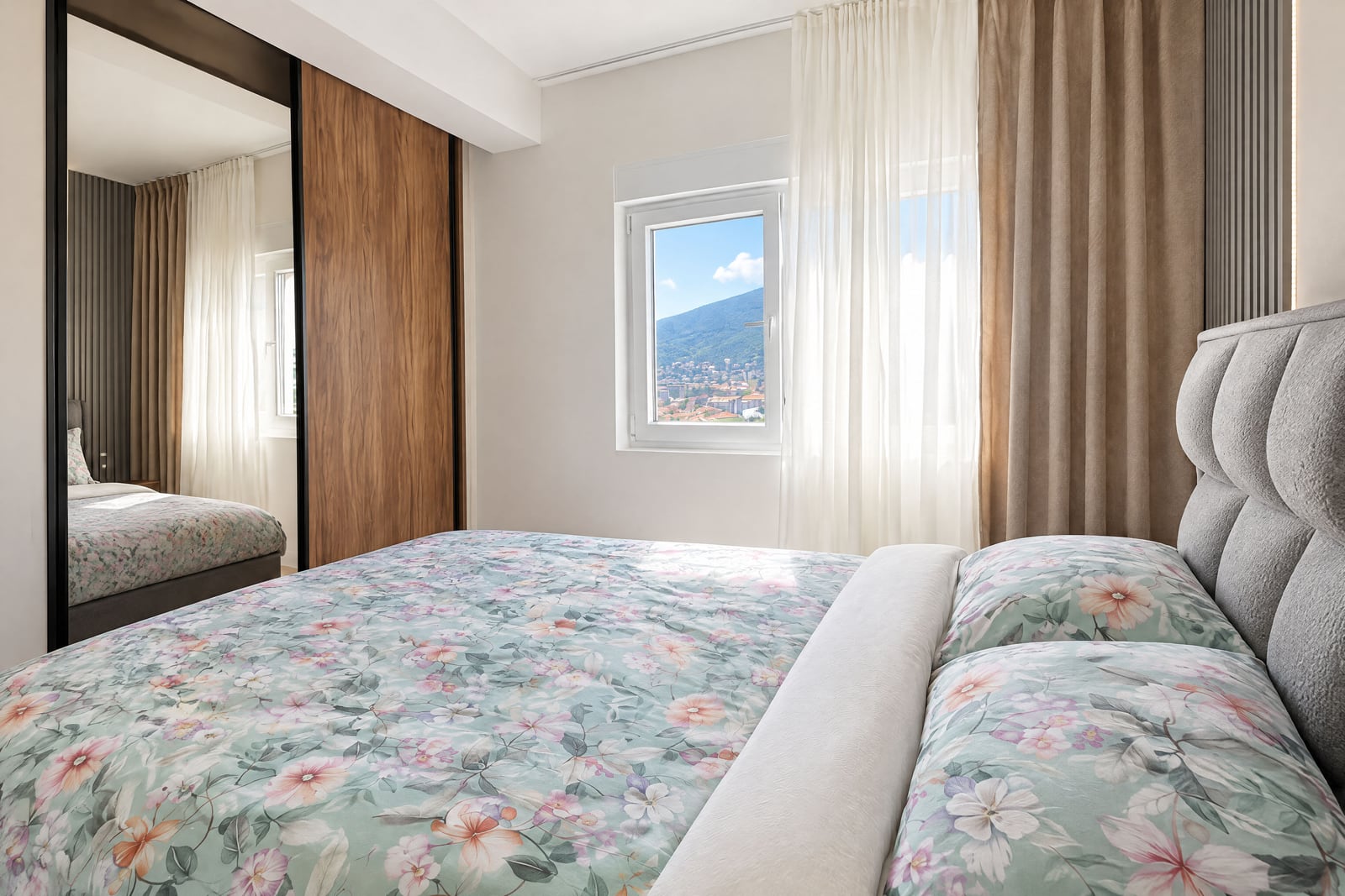Bedroom featuring a floral bedspread, wood wardrobe, and window overlooking a mountain cityscape.