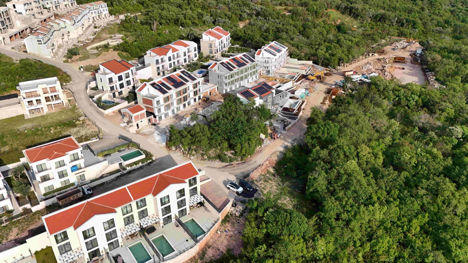 Aerial view of a residential complex under construction with swimming pools in Markovići, Montenegro, surrounded by forest.