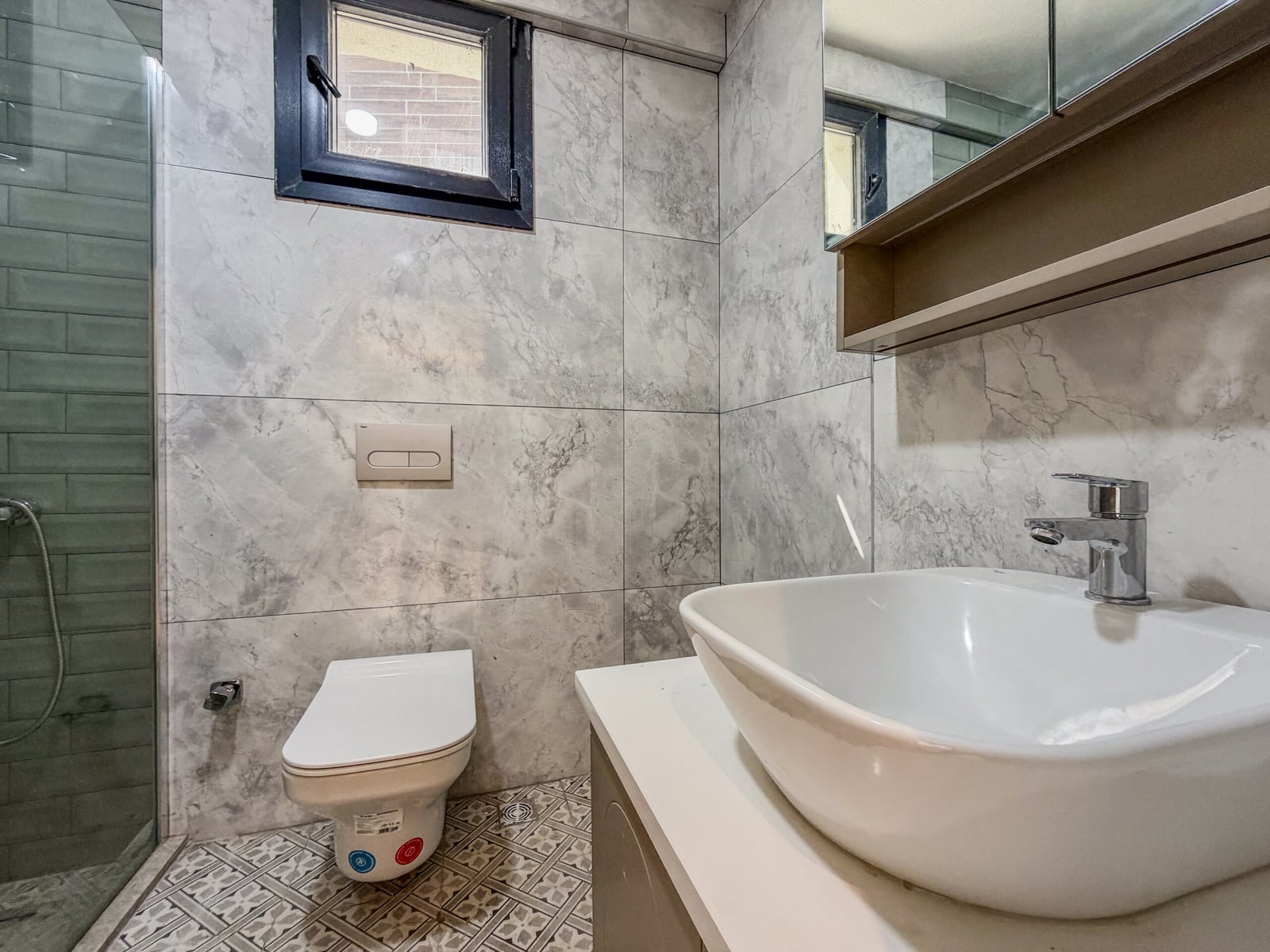 Bathroom featuring a wall-mounted toilet, vessel sink on a vanity, and a glass shower enclosure.