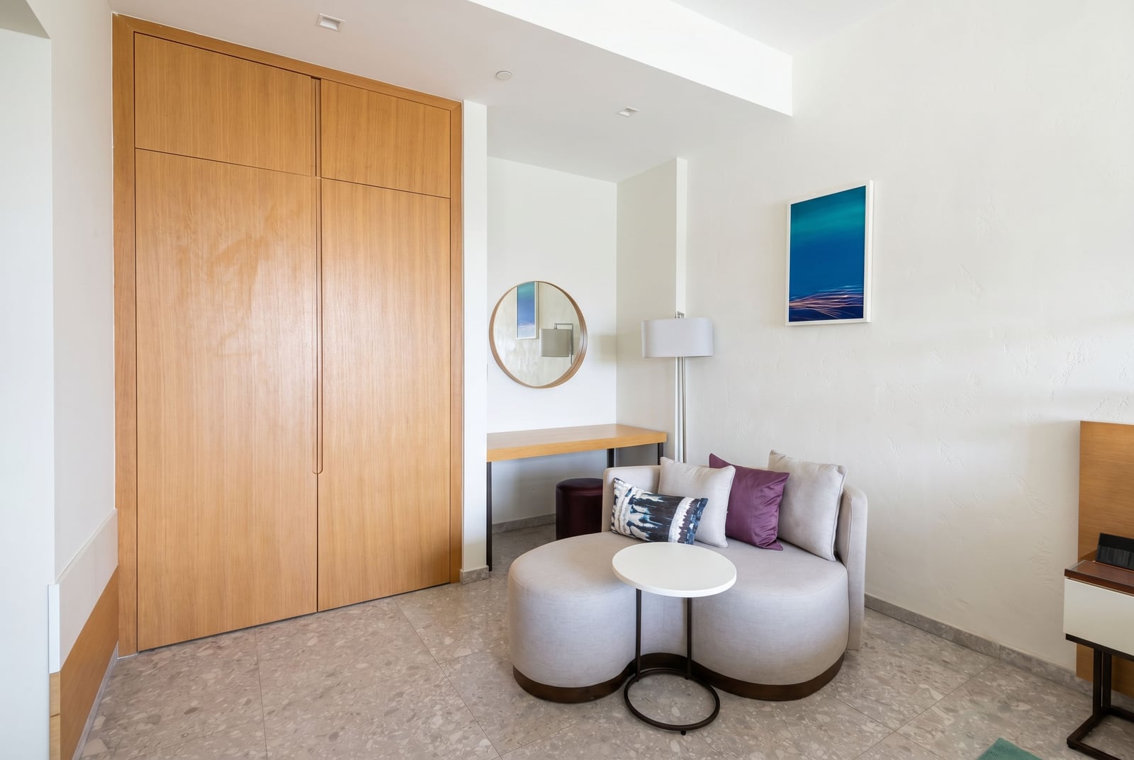 Modern bedroom at Lustica Bay hotel, Montenegro: light-colored furniture, built-in wardrobe, and a lounge area with an armchair.