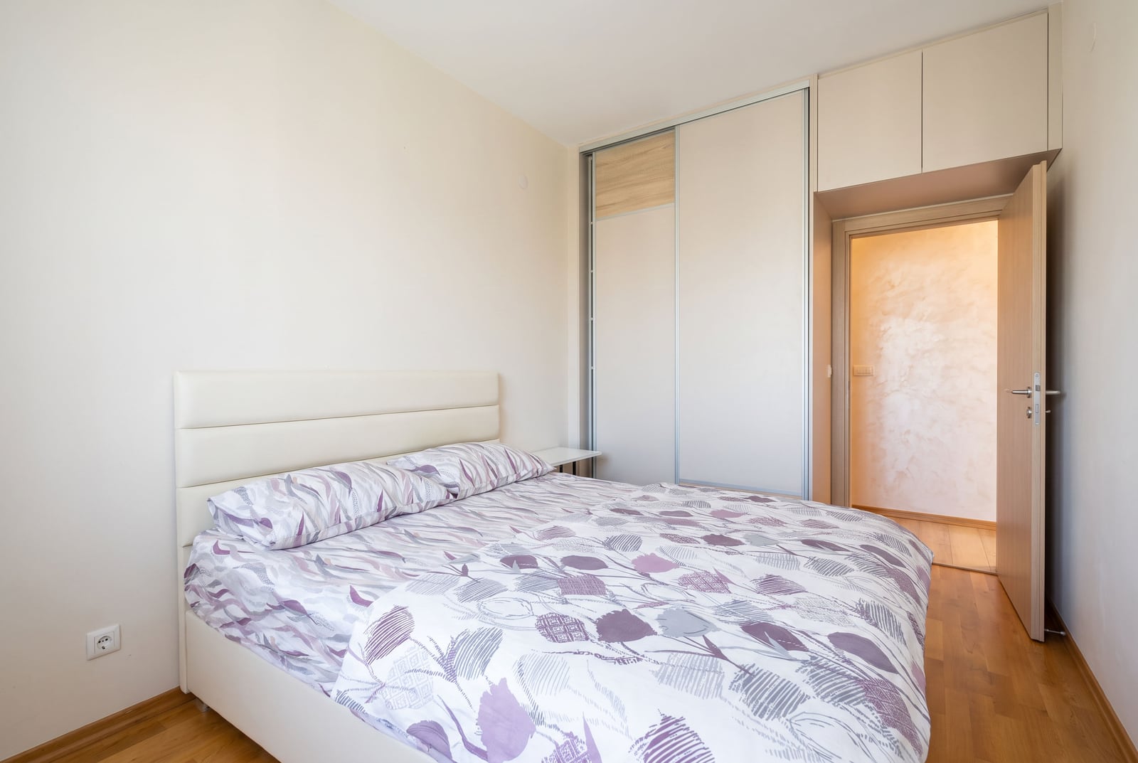 Bedroom featuring a double bed with floral bedding and a large sliding wardrobe unit.