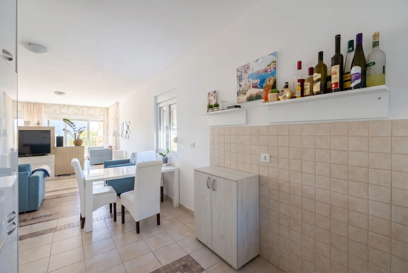 Living room with dining area, white table, blue sofas, and TV visible in the background.