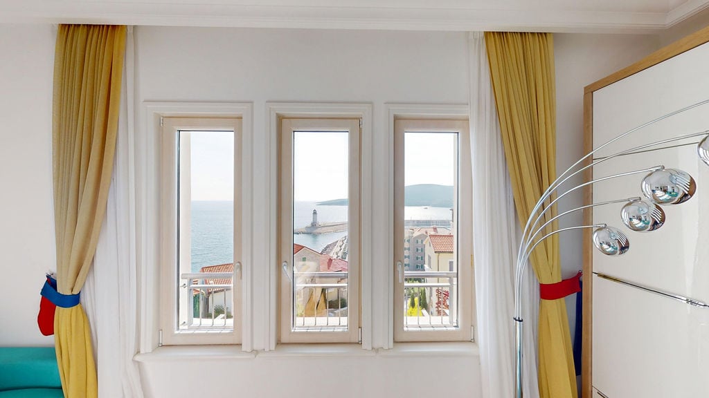 Sea and lighthouse view from the living room window in an apartment, Luštica, Montenegro: bright interior with yellow curtains.
