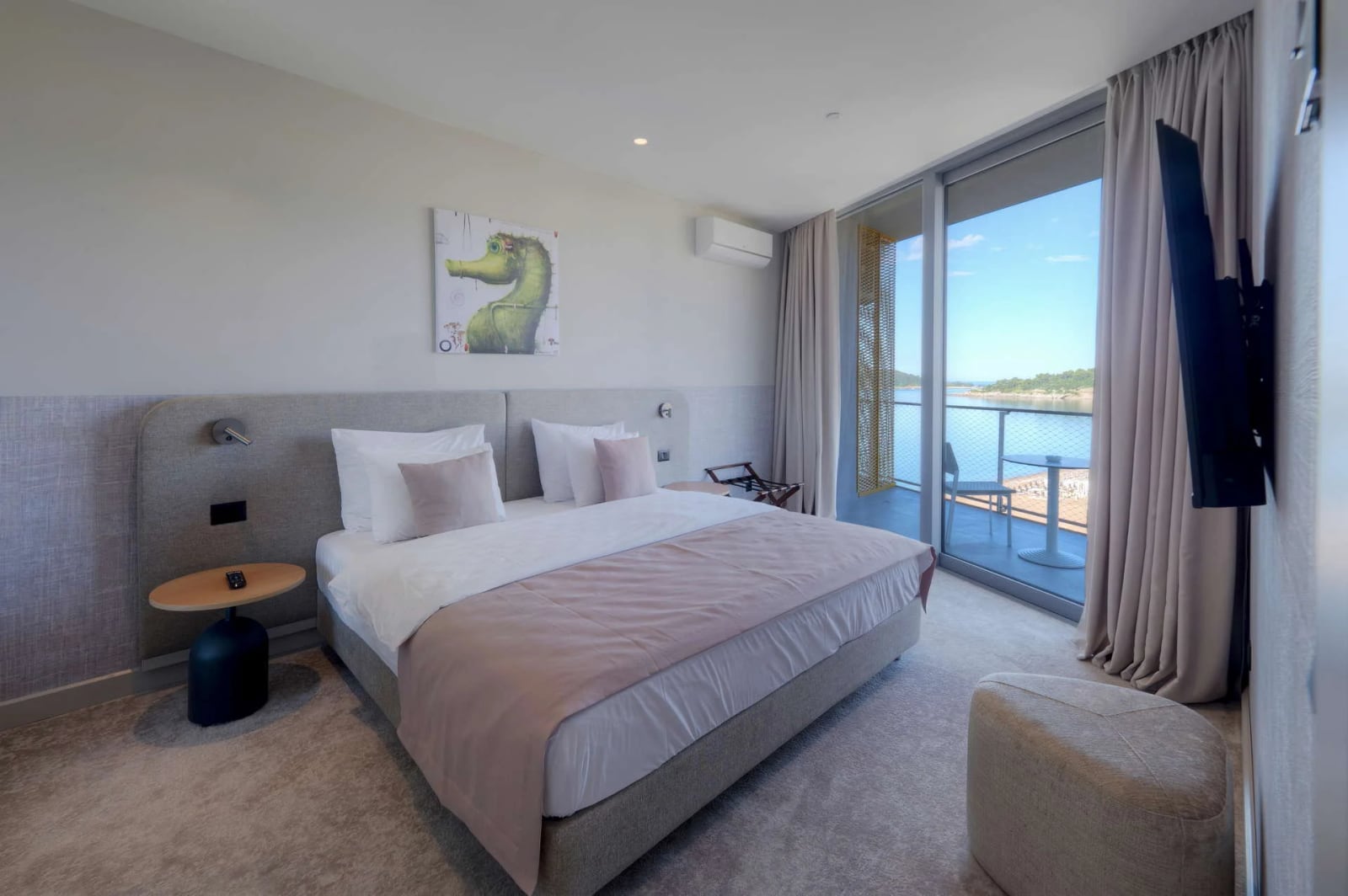 Modern bedroom with a double bed, wall art, and sliding glass doors leading to a balcony overlooking water.