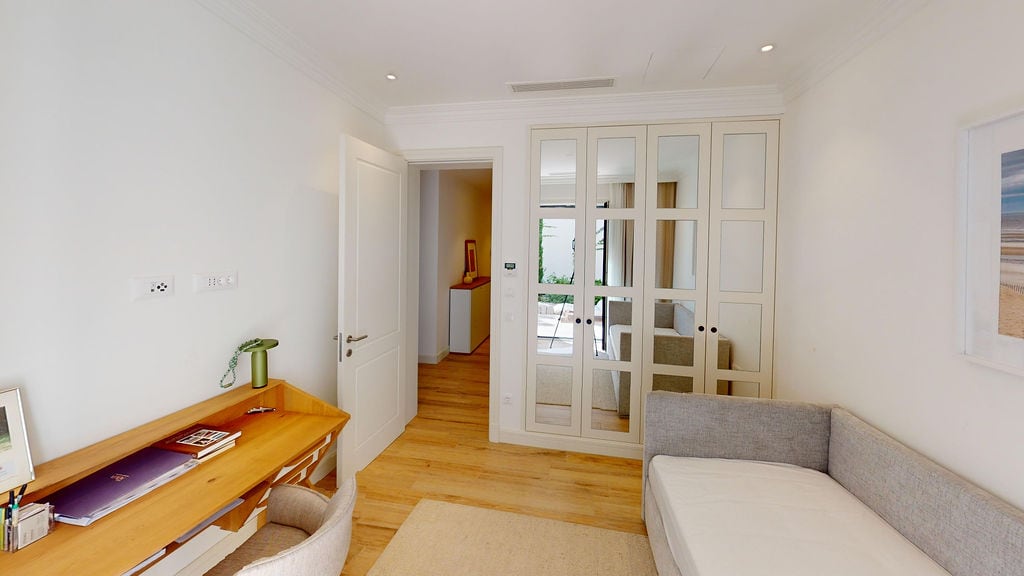Bedroom in an apartment in Luštica, Montenegro: bright interior, built-in mirrored wardrobe, wooden table, and sofa.