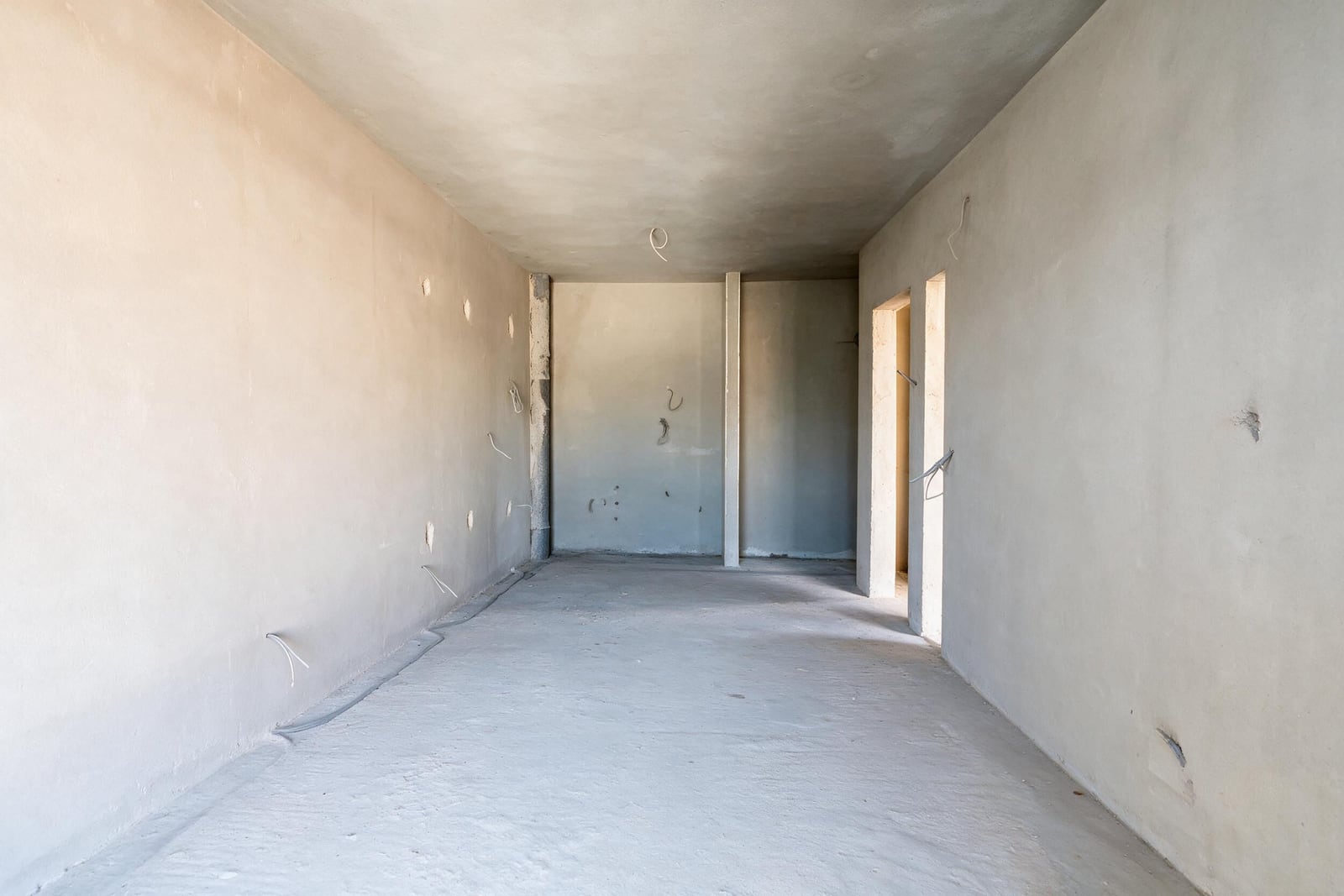 Unfinished interior with bare walls, concrete floor, and exposed electrical wires hanging from surfaces.
