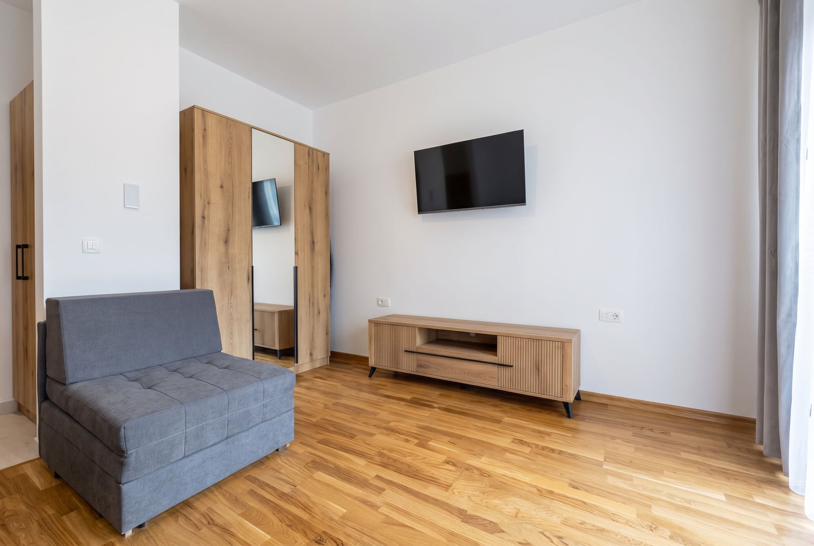 Modern bedroom with a gray sofa, TV area, and wardrobe in an apartment in Budva, Montenegro