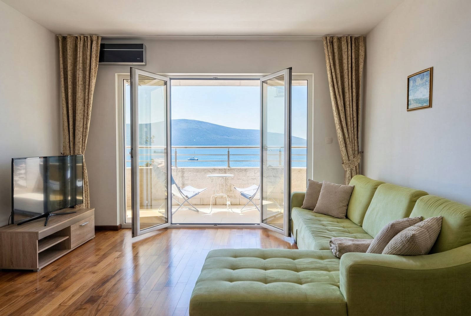 Living room with a green sofa and a terrace overlooking the sea in an apartment in Tivat, Montenegro.