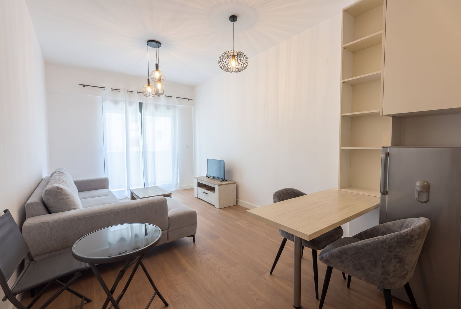 Living room featuring a grey sofa, TV unit, dining table, and pendant lights.