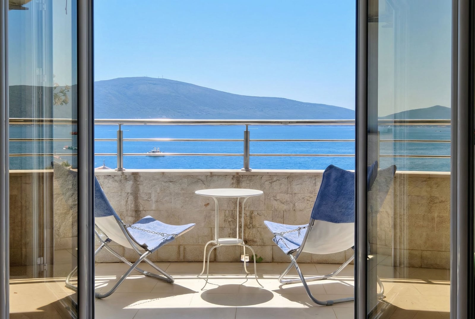 Balcony with furniture and panoramic sea and mountain views in an apartment in Tivat, Montenegro.
