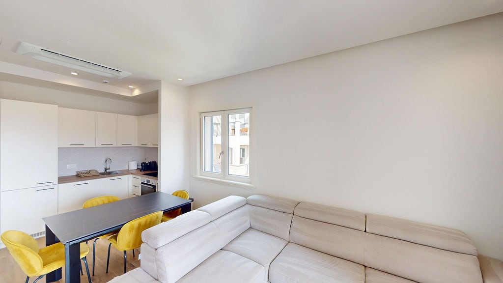 Modern living room with kitchen in an apartment in Luštica, Montenegro: beige sofa, dining table, and yellow chairs.