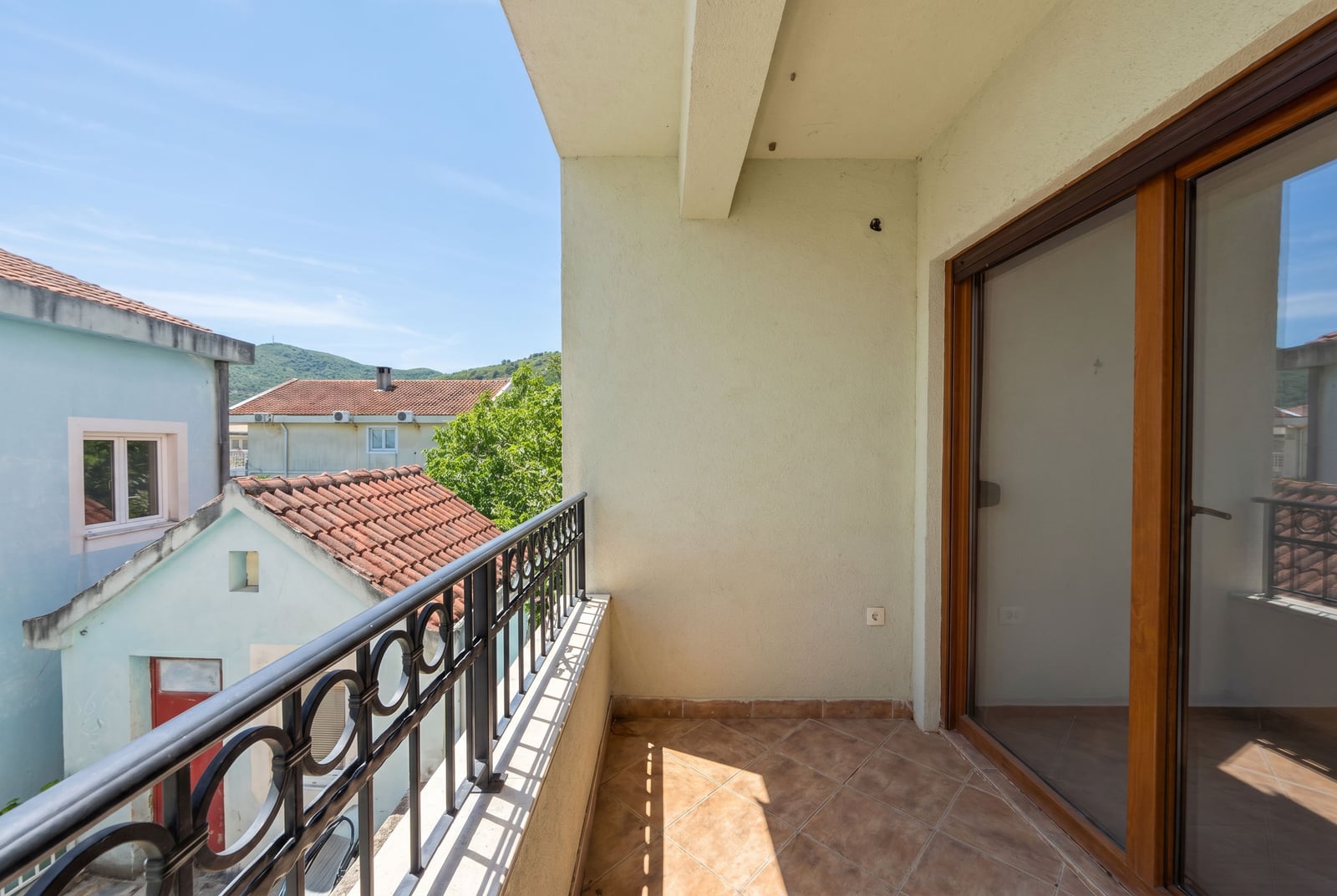 Open balcony with wrought iron railing and a view of houses and mountains in an apartment in Budva, Montenegro.