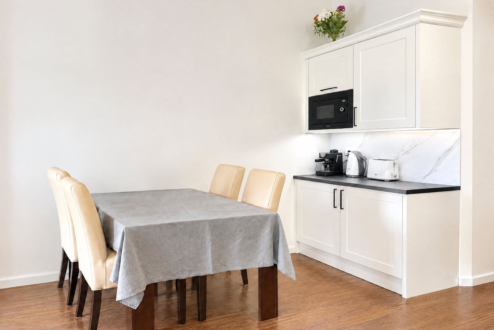Kitchen area with white cabinets, microwave, toaster, coffee maker next to a dining table.