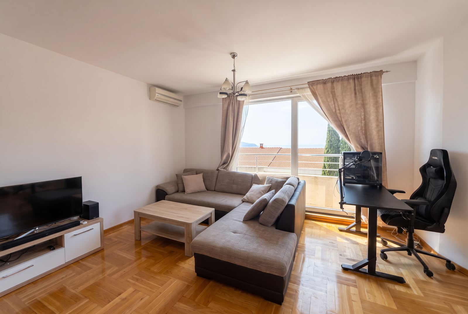 Spacious living room with a corner sofa, workspace, and TV in an apartment in Bečići, Montenegro.