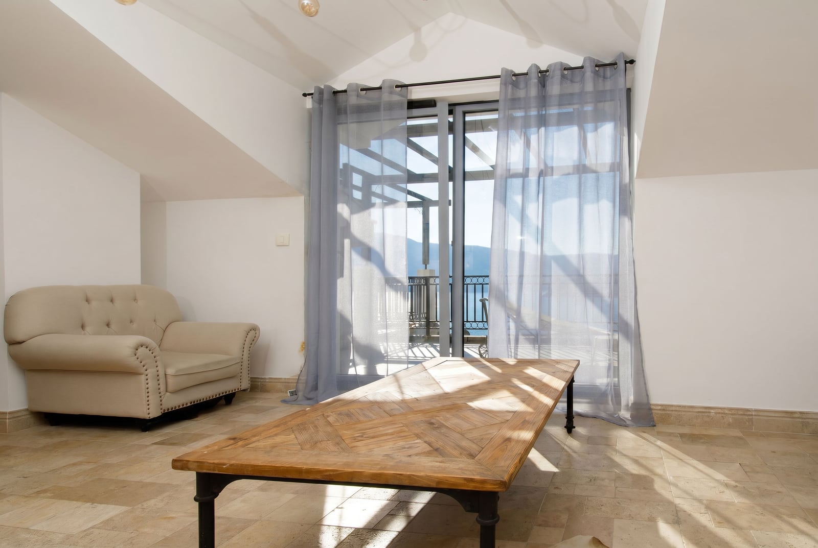Living room in a penthouse in Risan, Montenegro: a bright room with an armchair, a wooden table, and access to a terrace with a view.