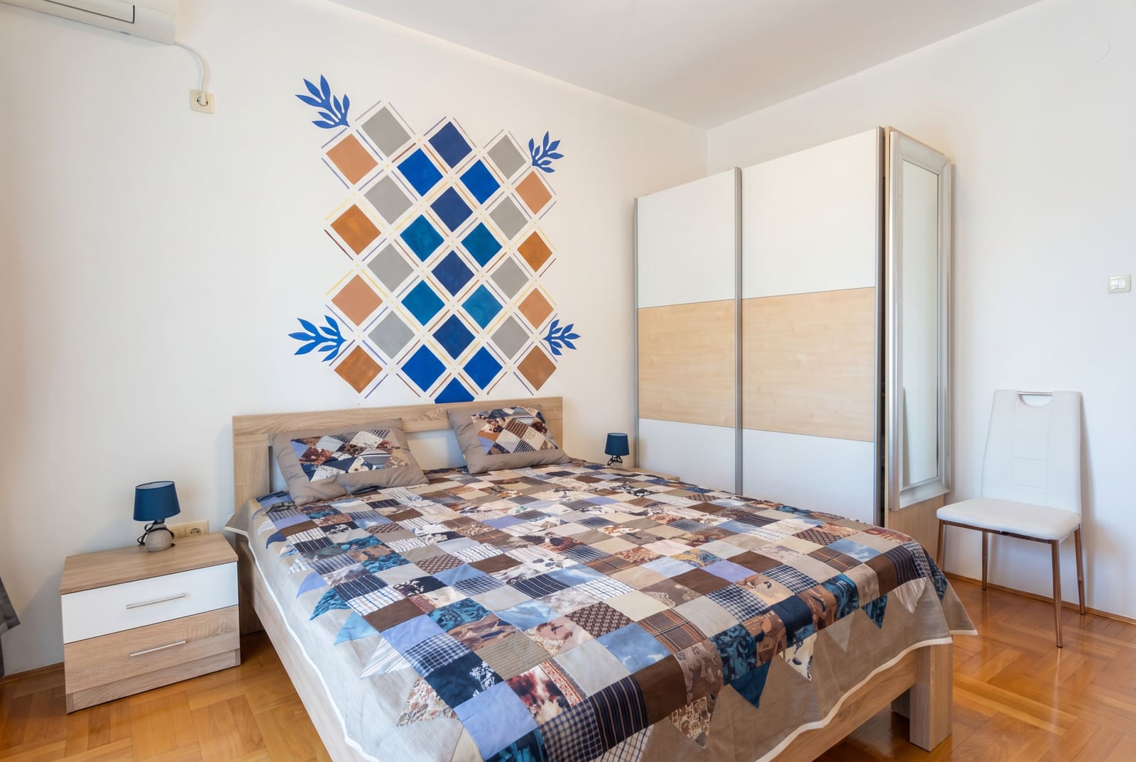 Bedroom in an apartment in Bečići, Budva, Montenegro: double bed, sliding wardrobe, and patchwork-style wall decor.
