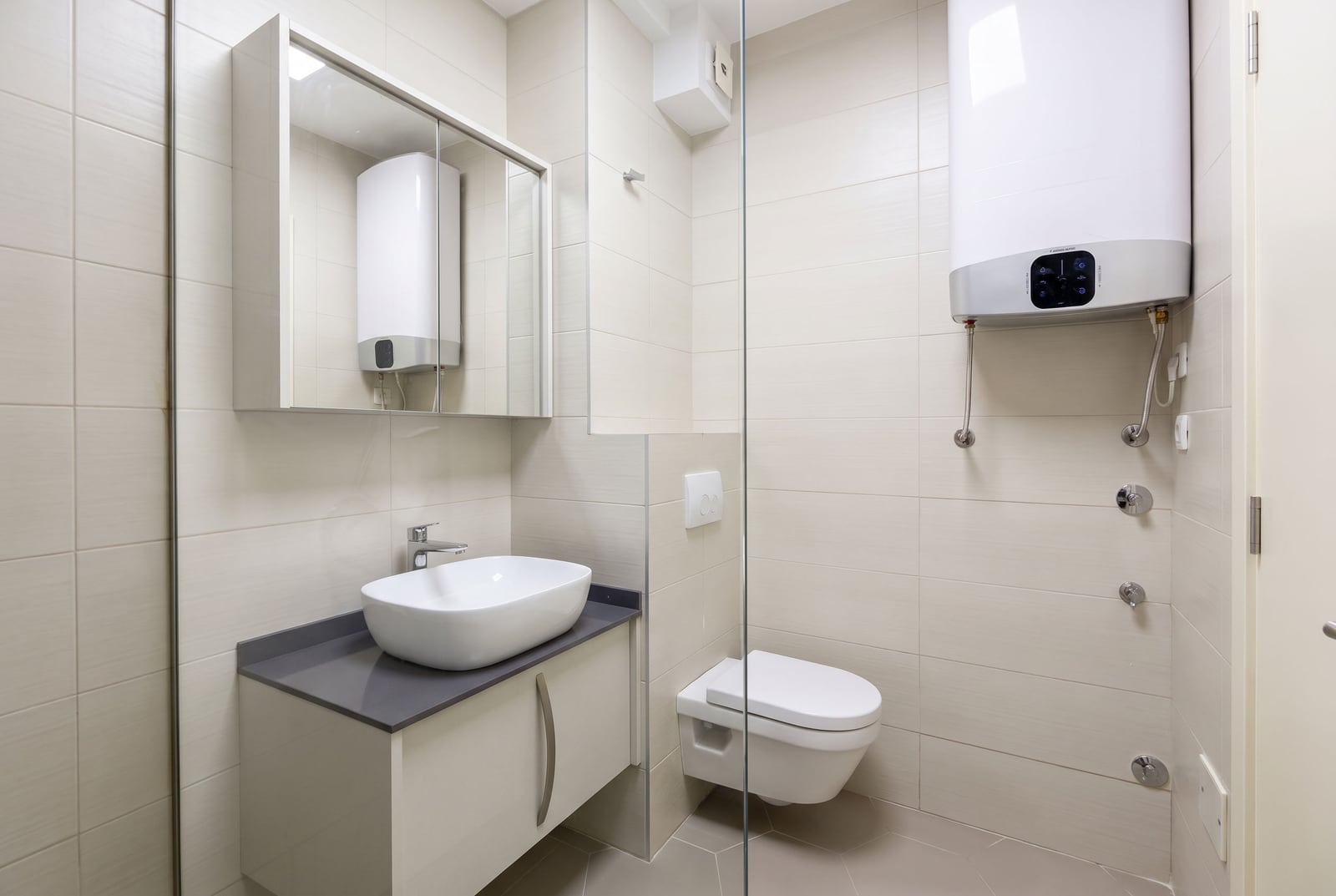 Modern bathroom with a shower cabin and water heater in an apartment, Dobrota, Montenegro. Light-colored tiles and sanitary ware.