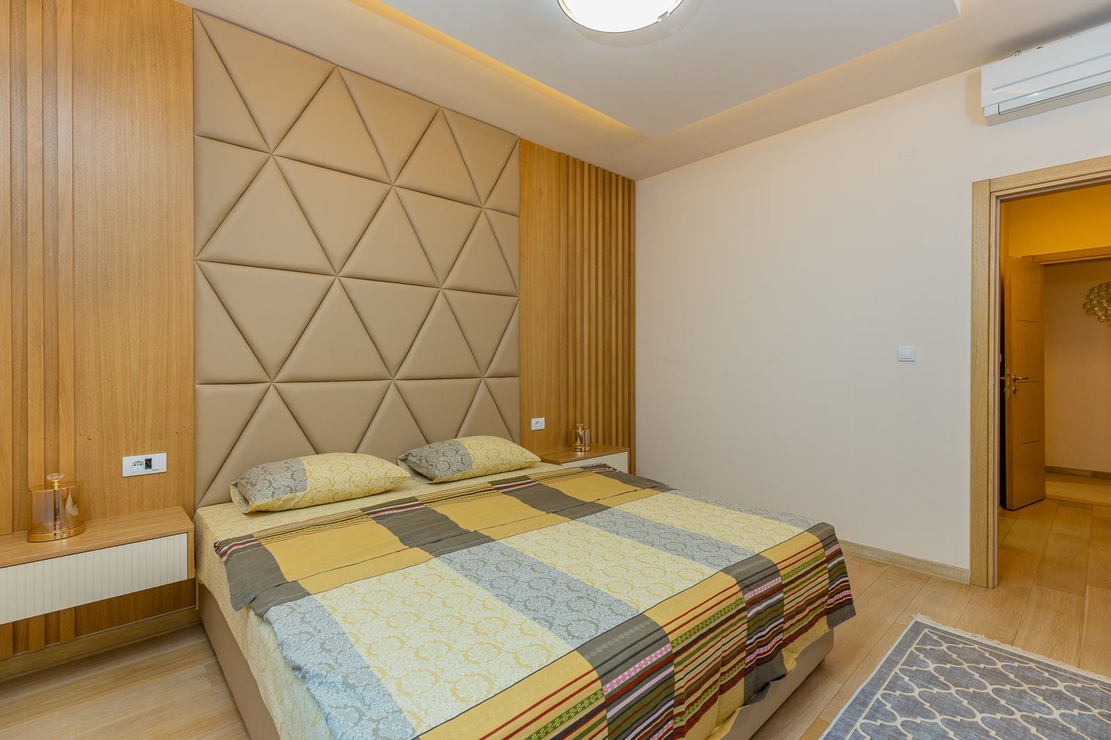 Modern bedroom in a penthouse in Pržno, Montenegro: a double bed, upholstered headboard, and stylish wood finishes.