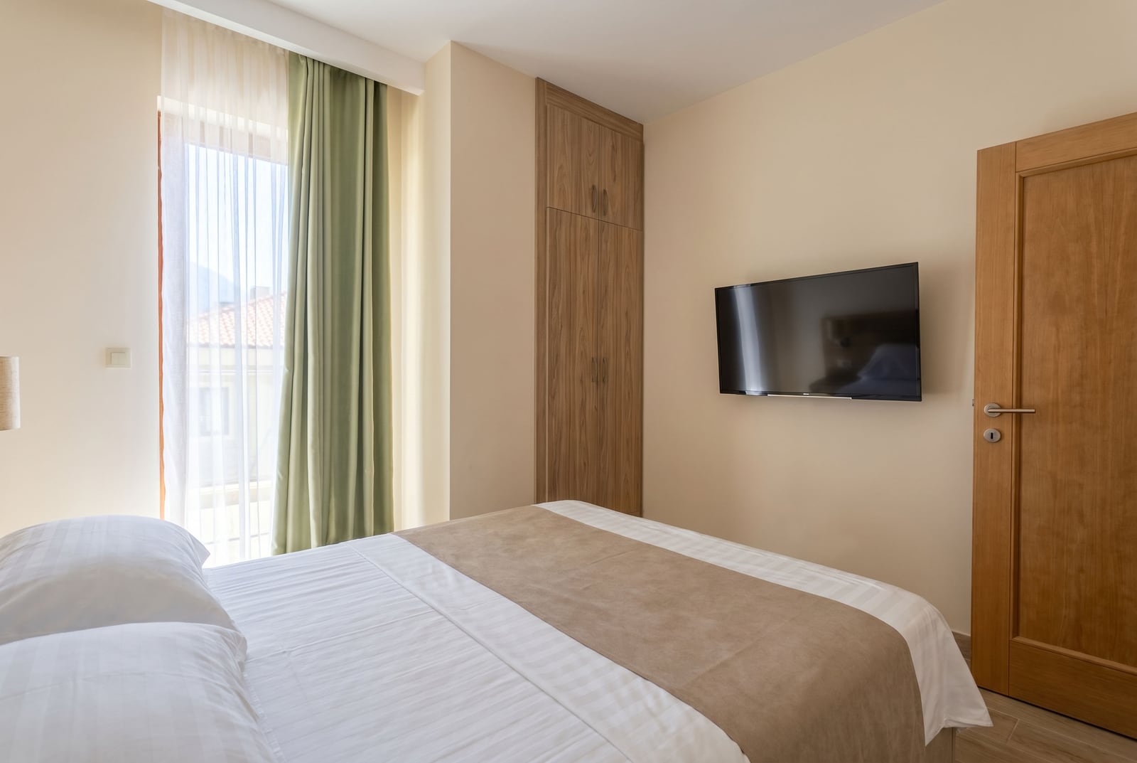 Modern bedroom in an apartment in Bečići, Montenegro: double bed, built-in wardrobe, and TV on the wall.