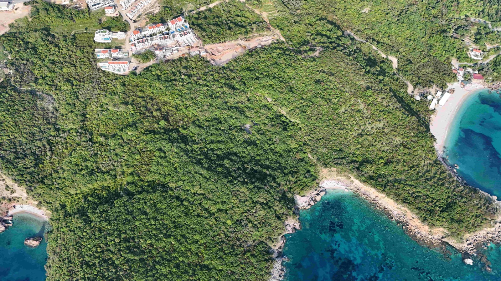 Aerial view of a land plot in Reževići, Montenegro: a green area by the sea with a beach and residential development.