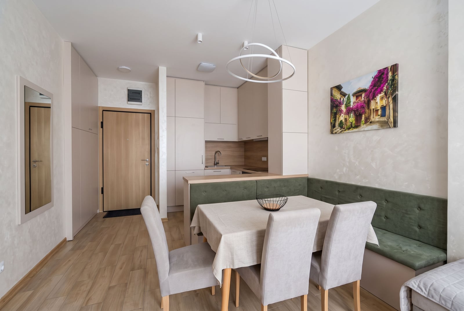 Dining area with green banquette and table, partial kitchen view and entrance door visible.