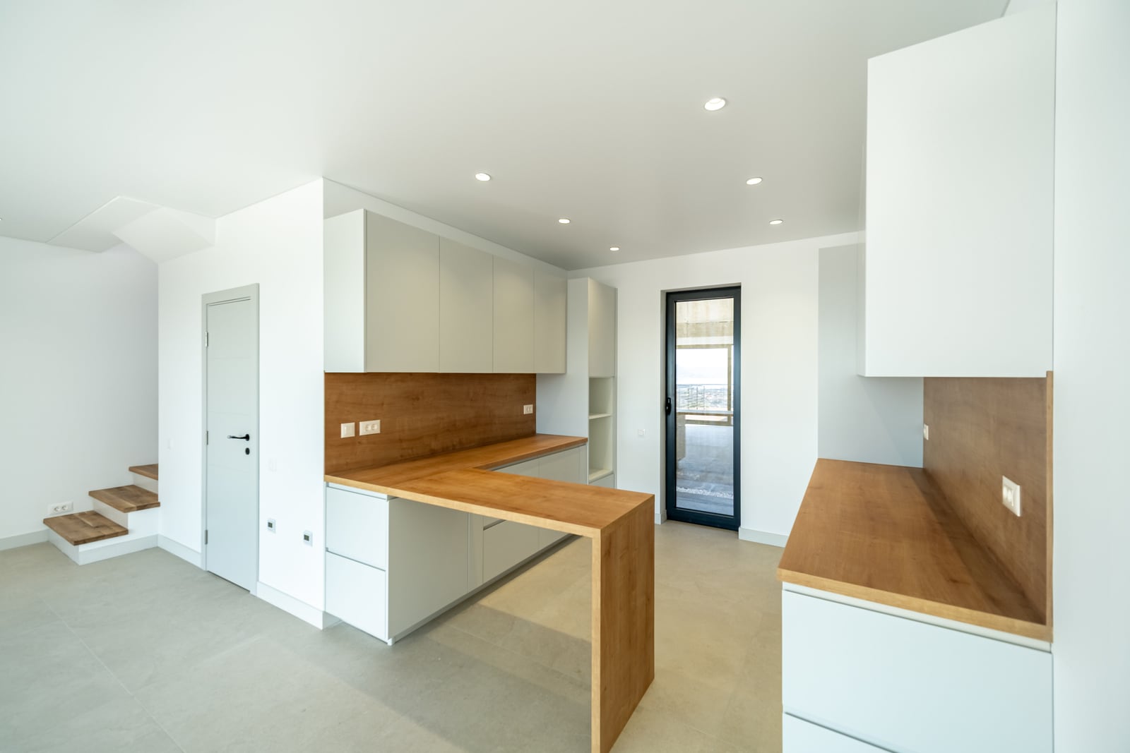 Modern kitchen in a townhouse in Kavač, Montenegro: light-colored cabinetry, wooden countertop, and access to the terrace.