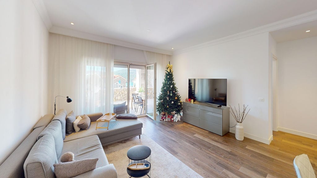 Bright living room with a gray sofa and TV area in an apartment at Luštica Bay, Montenegro. Access to a terrace with mountain views.