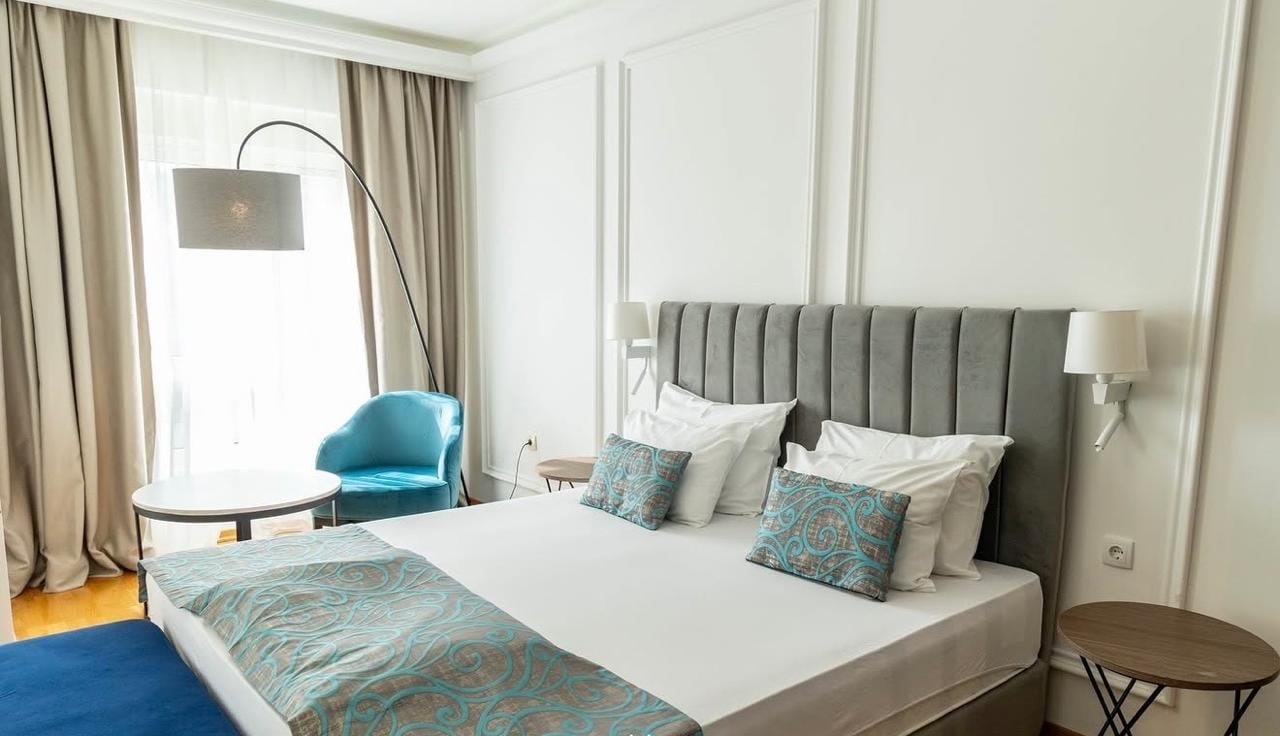 Modern bedroom in an apartment in Bečići, Montenegro: double bed with a grey headboard and a blue armchair by the window.