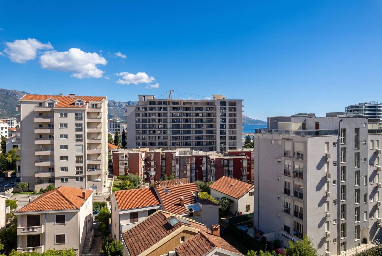 Panoramic view of city blocks and the sea in Budva, Montenegro, from modern residential buildings and tiled roofs.