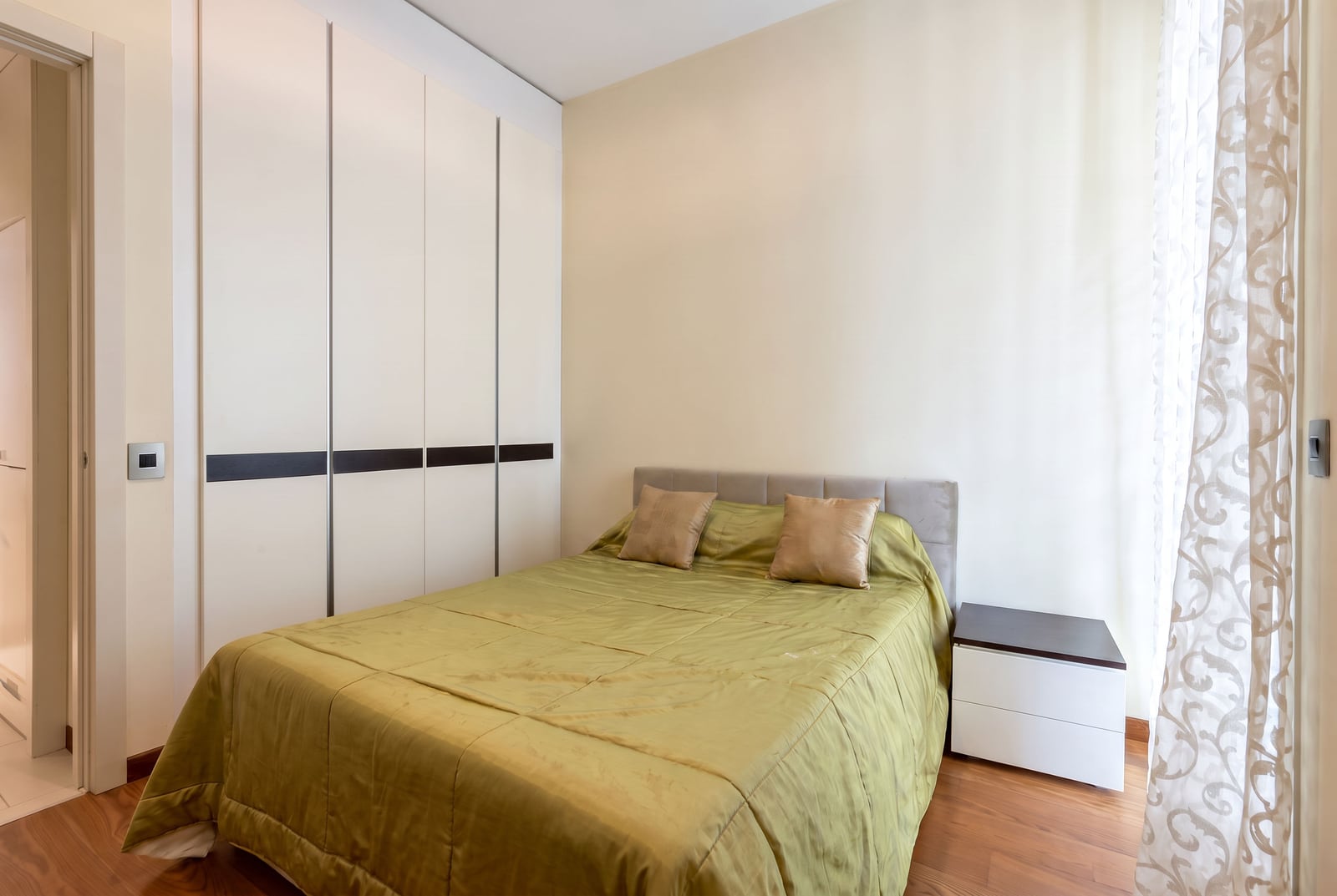 Bedroom featuring a bed with green bedding, white sliding wardrobe, nightstand, and wooden flooring.