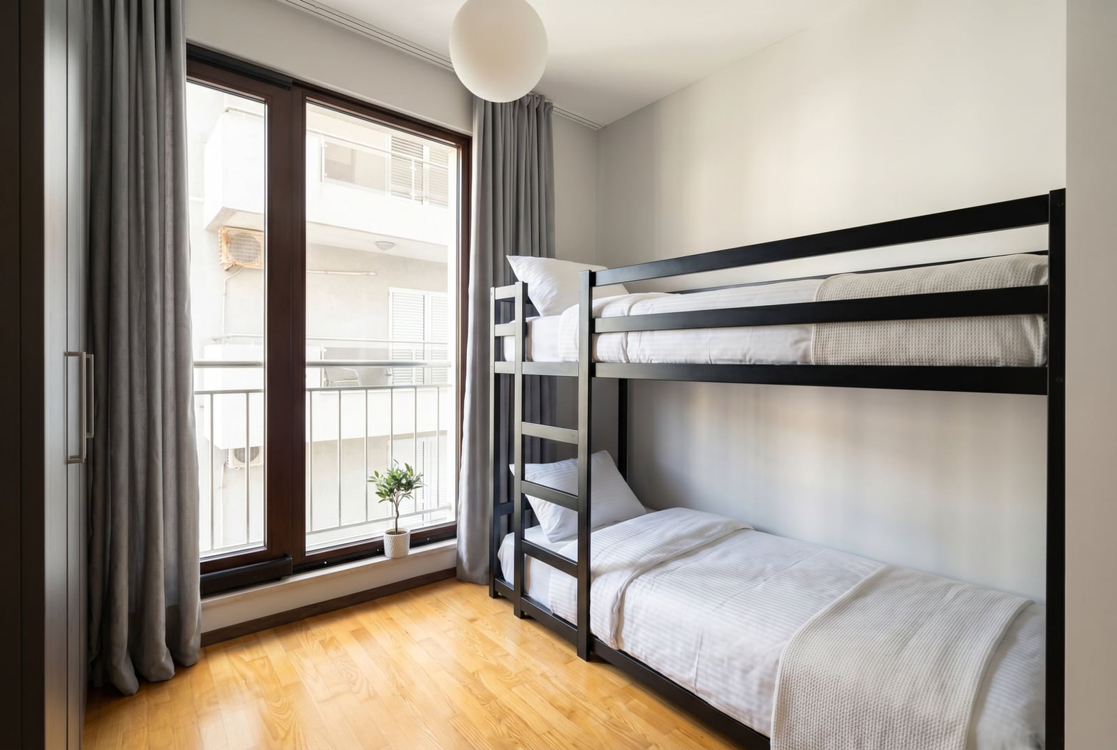 Bedroom with a bunk bed in an apartment in Budva, Montenegro: bright interior, panoramic window, and parquet flooring.