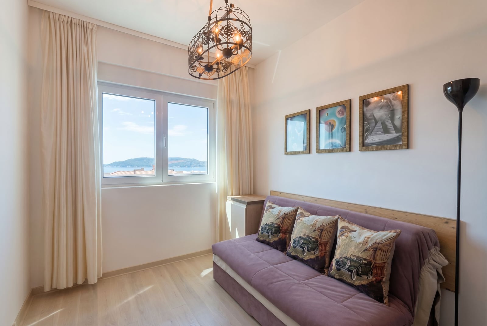 Living room with a sofa and sea view in an apartment in Becici, Montenegro: bright interior, stylish chandelier, and decor.