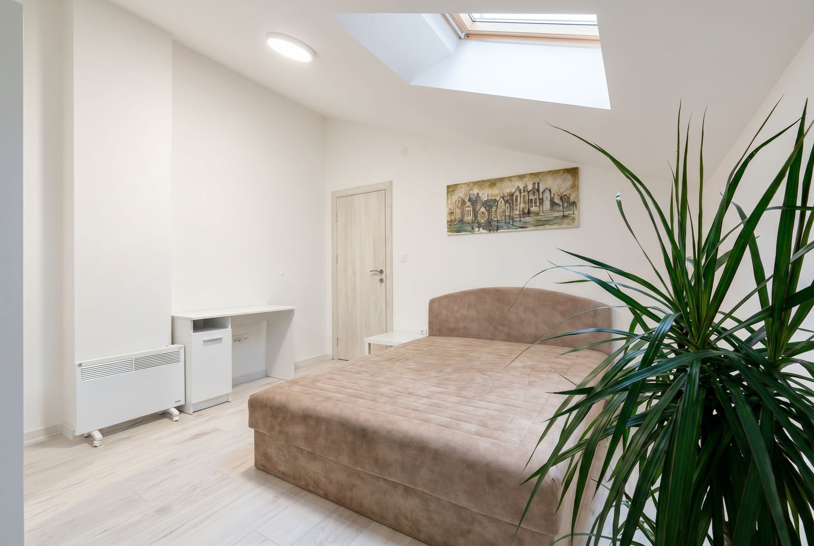 Bright bedroom in an apartment in Budva, Montenegro: double bed, skylight, desk, and houseplant.