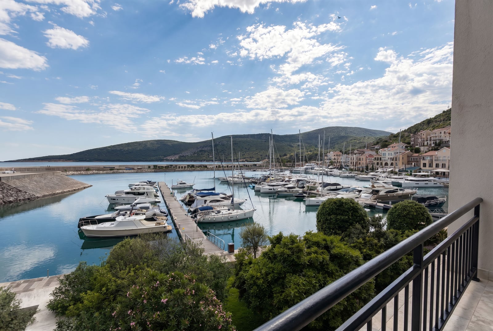 Balcony view of the marina with yachts in Luštica Bay, Montenegro: panoramic view of the bay, the pier, and mountains in the background.
