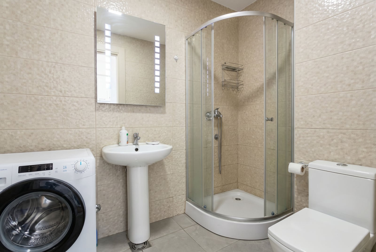 Modern bathroom with a shower cabin, sink, washing machine, and toilet in an apartment in Budva, Montenegro