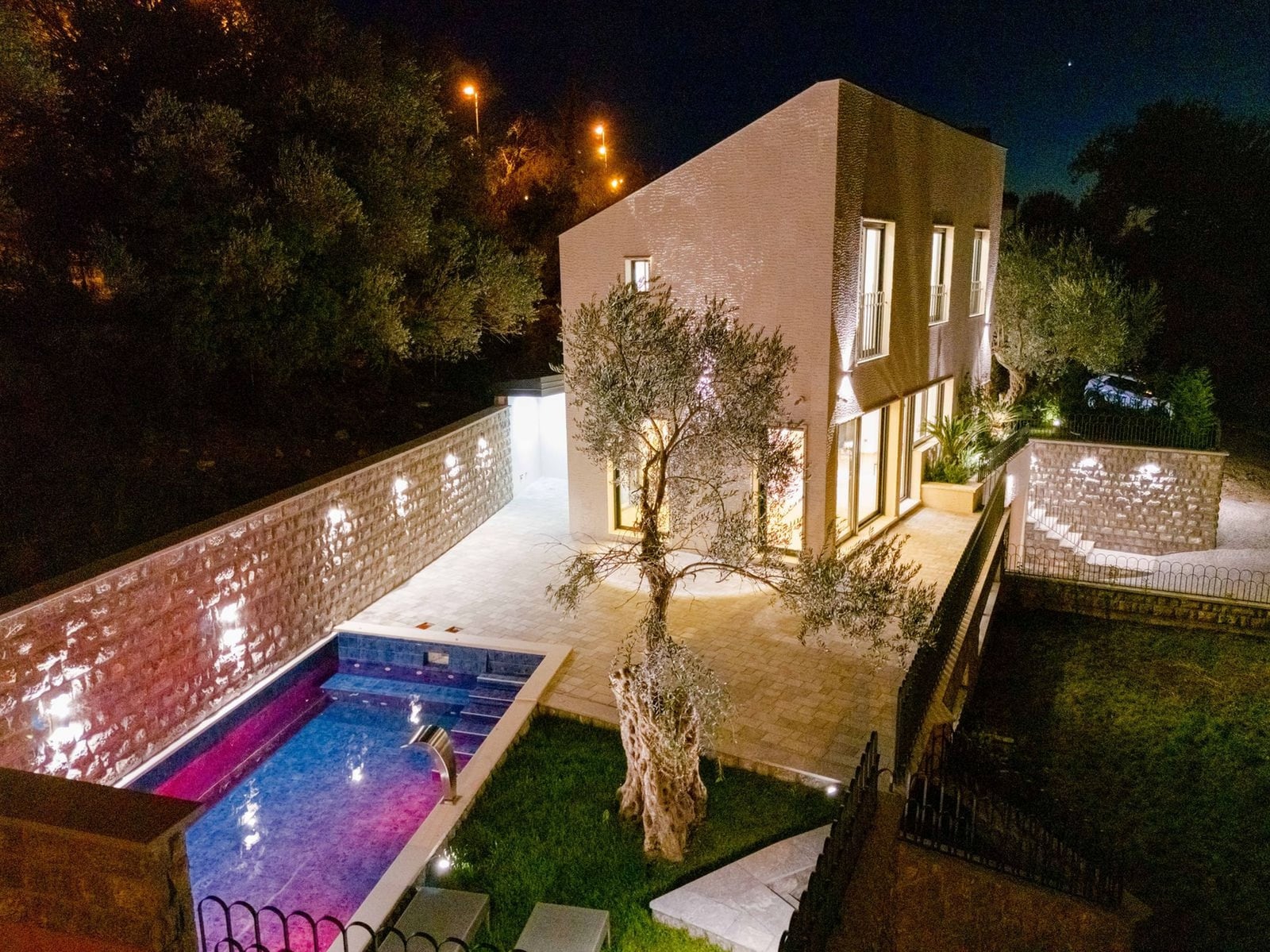 Modern villa in Kamenovo, Montenegro: night view of the house with a pool, terrace, and an olive tree in the garden.