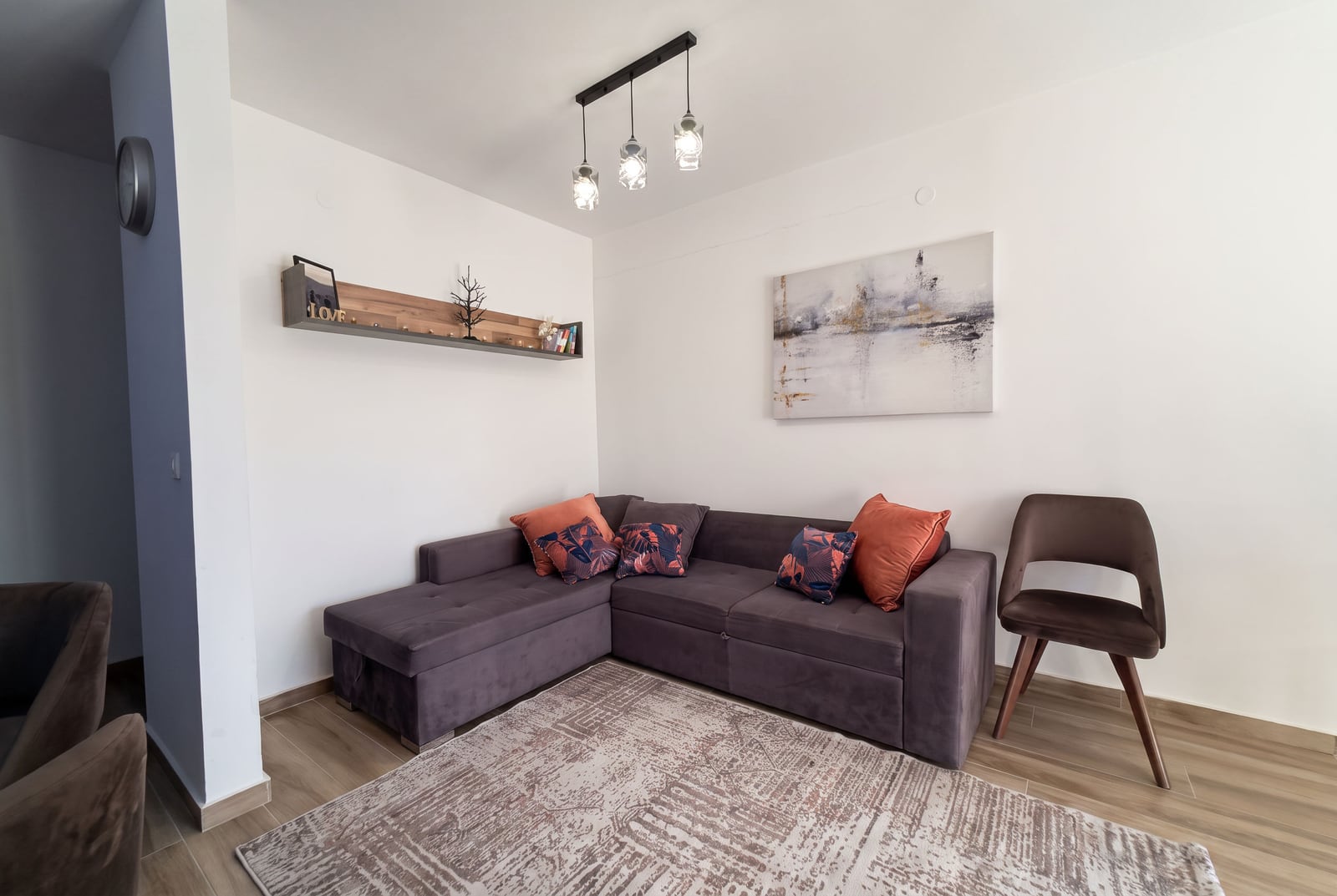 Living room featuring a purple sectional sofa, patterned rug, pendant lights, and abstract wall art.