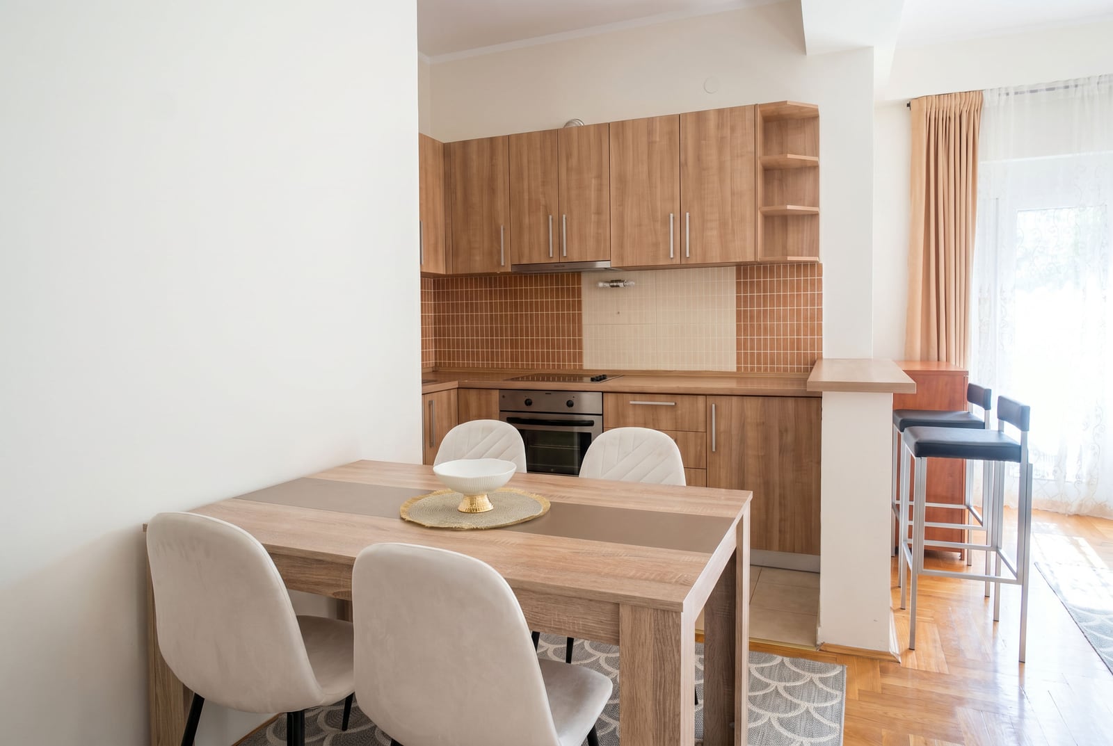 Modern kitchen with a dining area in a Budva apartment, Montenegro: wooden cabinetry, a breakfast bar, and light-colored chairs.