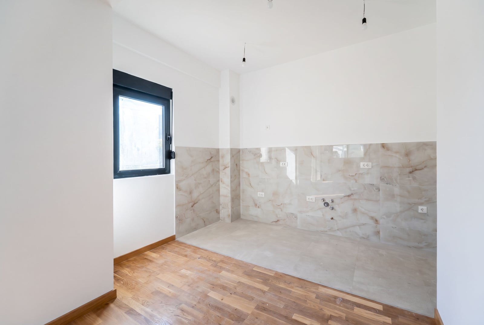 Kitchen without furniture with white walls, marble backsplash, and utility connections in a new development in the city of Bar, Montenegro